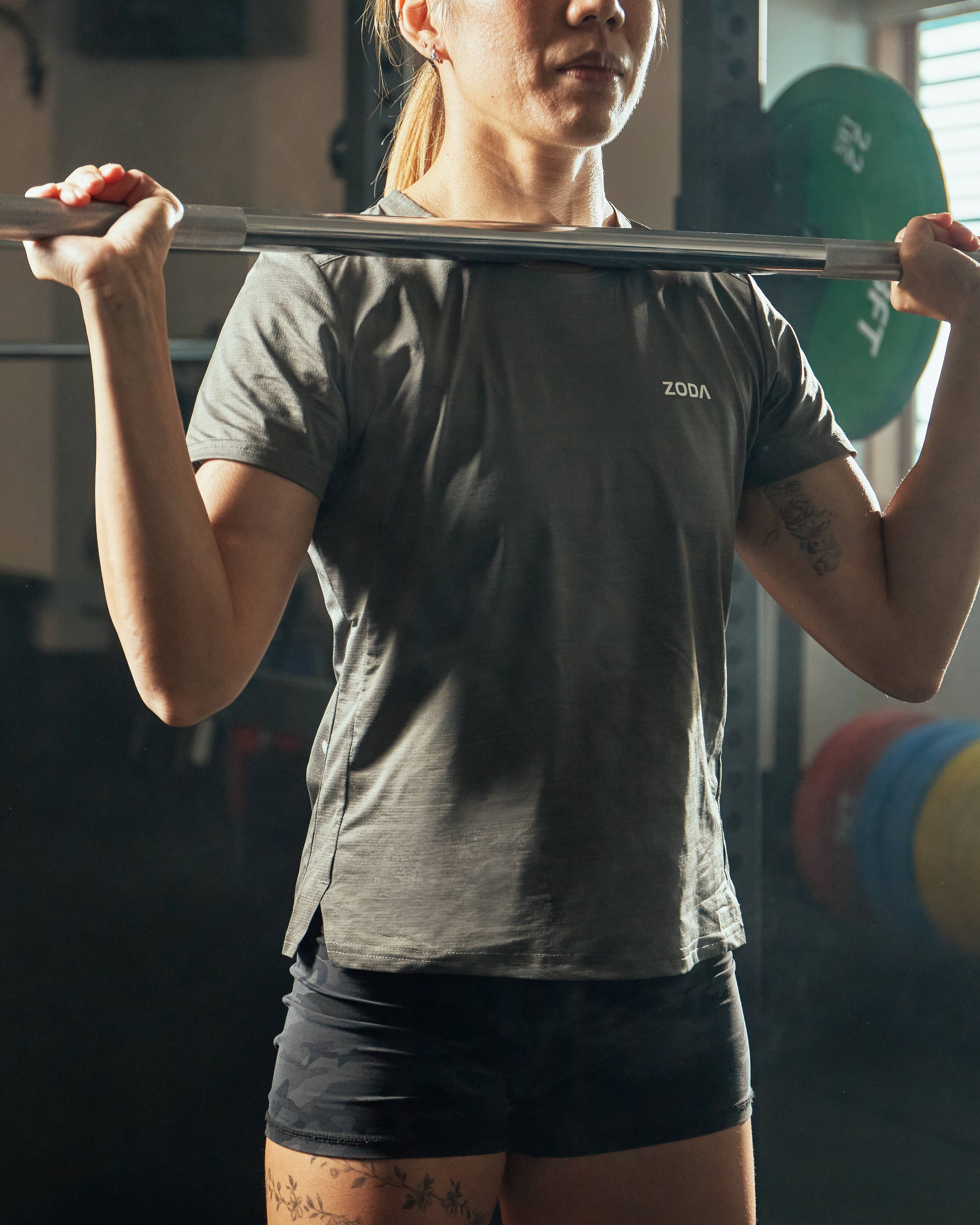 A woman lifting a barbell wearing a gray t-shirt and black shorts.