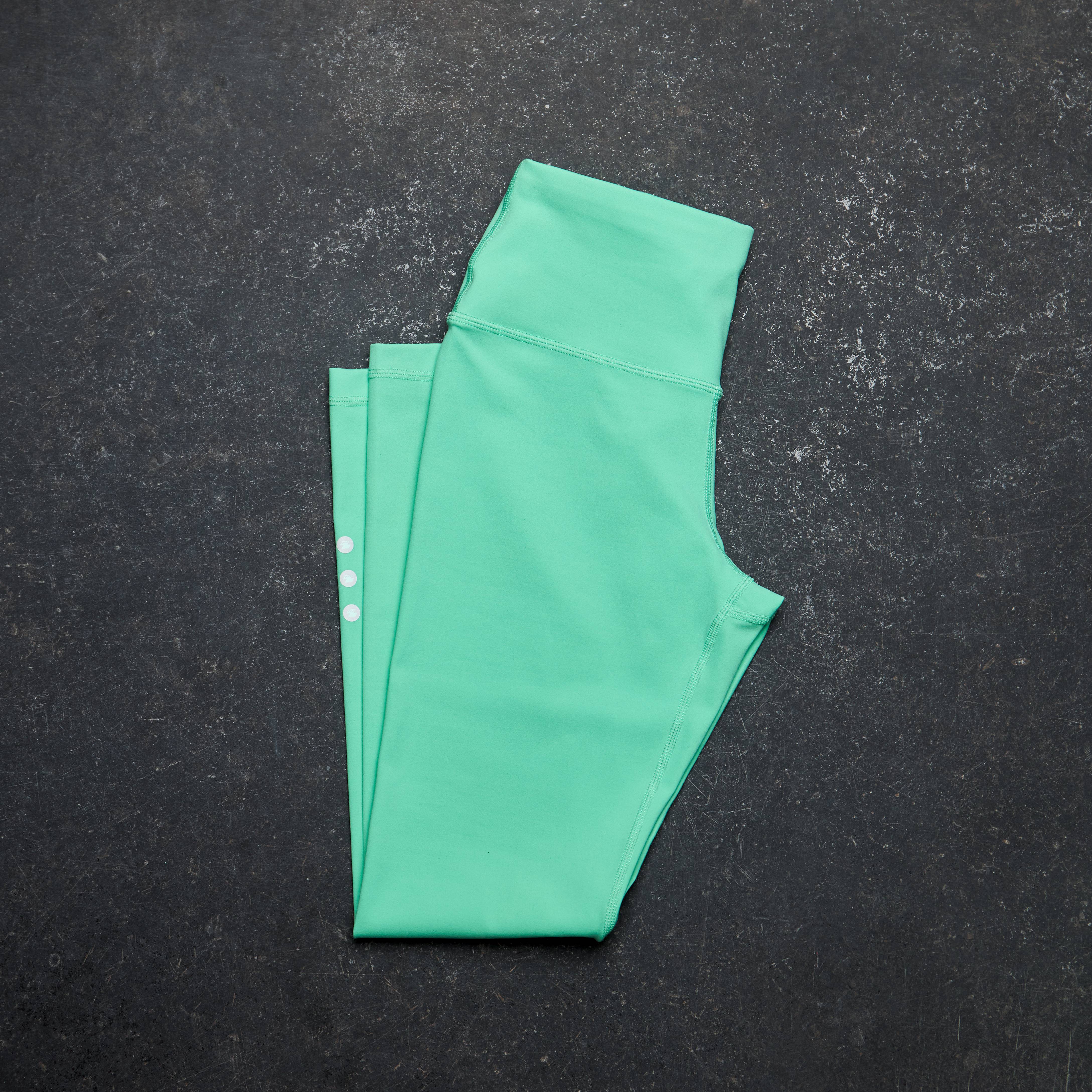 Green leggings folded on a dark textured surface Zoda.sg