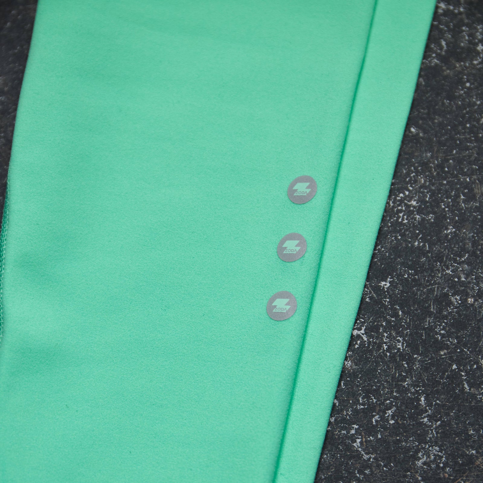 Green fabric with button details on a textured black surface Zoda.sg