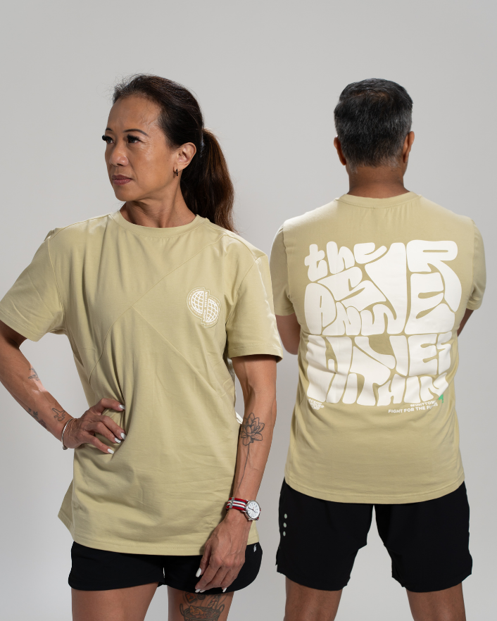 Two adults, one male and one female, wearing pale olive colored oversized tees with text graffiti print on the back, standing back to back. Performance wear - Zoda.sg In it to win it, Singapore
