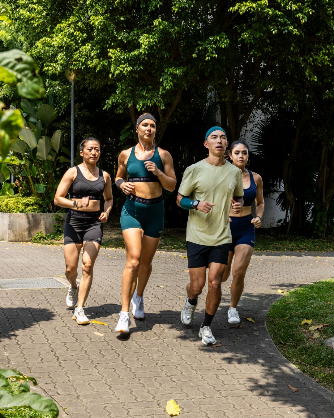 Four people running outdoors on a paved path with greenery in the background Zoda.sg