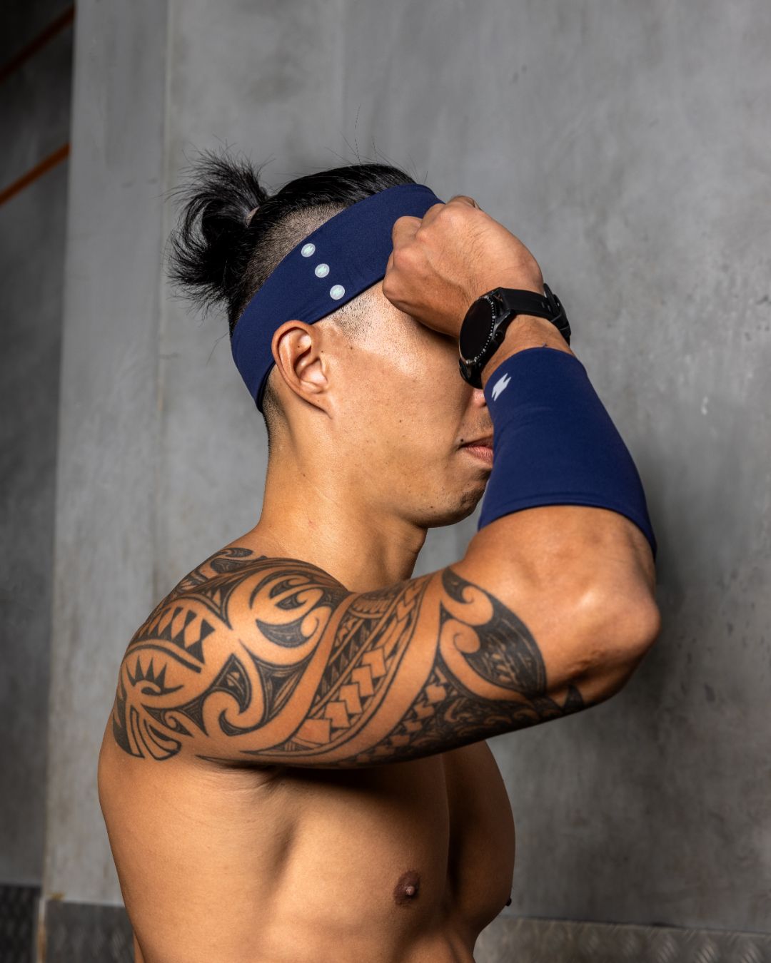 Man with tribal tattoos wearing a blue headband and wrist wrap against a gray background Zoda.sg