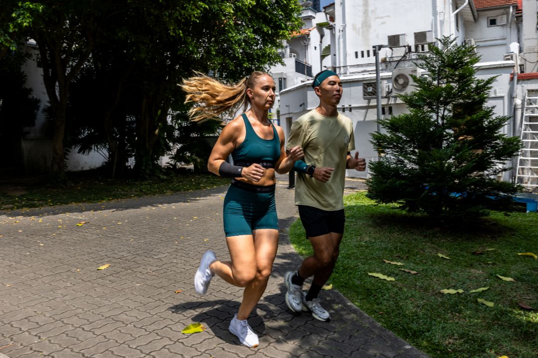Two people running on a paved path with buildings and trees in the background Zoda.sg