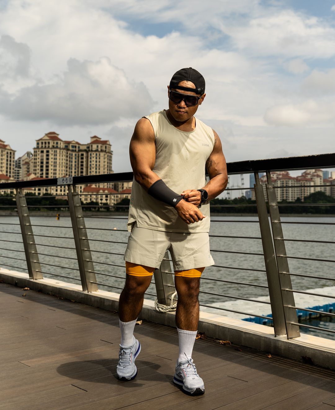 Man in athletic wear standing by a waterfront with buildings in the background Zoda.sg