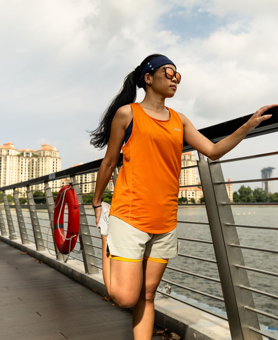 Zoda.sg Woman in athletic wear standing on a bridge with a cityscape in the background