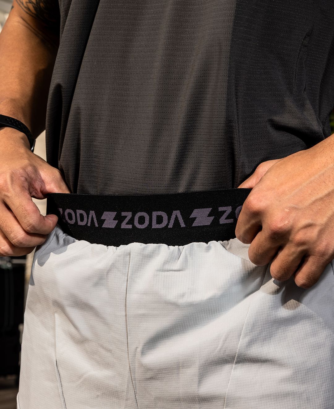 Person wearing a black belt with 'ZODA' branding, holding it with both hands. Zoda Pulse Collection