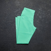 Green leggings folded on a dark textured surface Zoda.sg