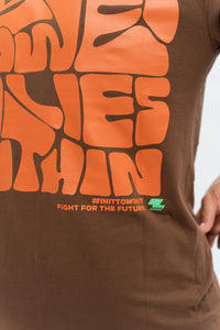 Close-up of a brown oversized t-shirt with orange text and a graphic design. Cozterra Zoda.sg