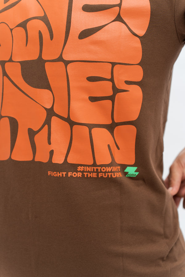 Close-up of a brown oversized t-shirt with orange text and a graphic design. Cozterra Zoda.sg