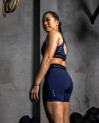 Woman wearing a blue sports bra and shorts set against a gray wall. Zoda.sg